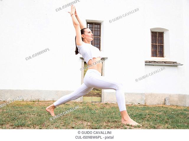Woman practicing yoga, warrior pose in front of building