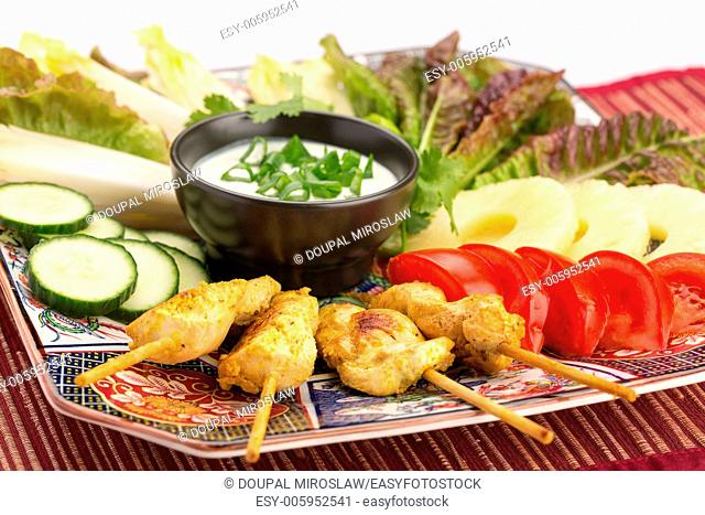 Asian food with chicken skewers, sauce, tomatoes, cucumber, pineapples, endives and salad