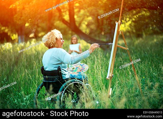 Inspired Disabled Woman Draws Her Charming Young Daughter In Park. Blurred Young Girl On The Background. Family Rest. Recovery