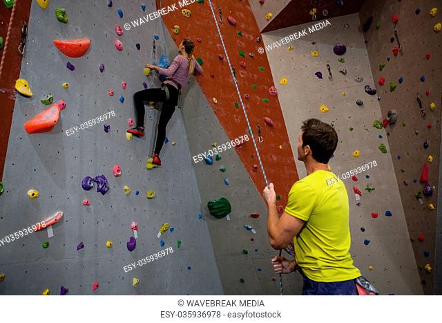 Man holding rope looking at athlete climbing wall in fitness studio