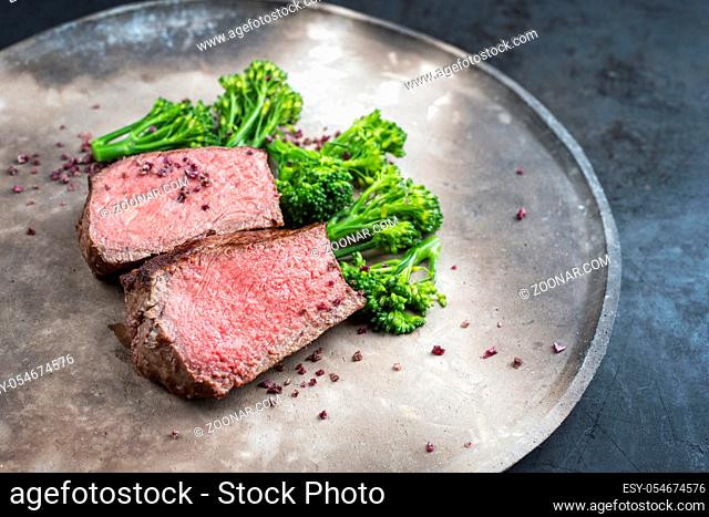 Barbecue dry aged wagyu roast beef natural sliced offered with rapini and salt as closeup on a modern design plate with copy space right