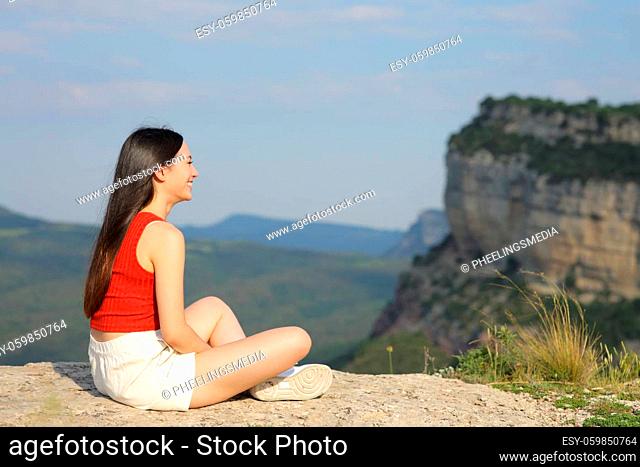 Full body portrait of an asian woman contemplating views sitting in a mountain cliff