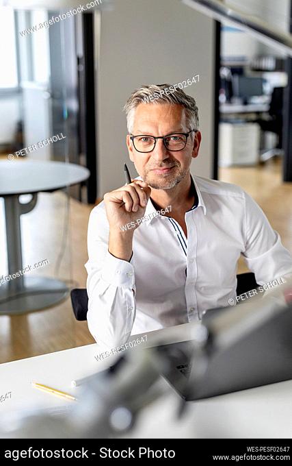Male entrepreneur holding pen while sitting at desk in office