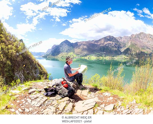 Italy, Lombardy, spring at Lake Idro, hiker sitting with map at observation point
