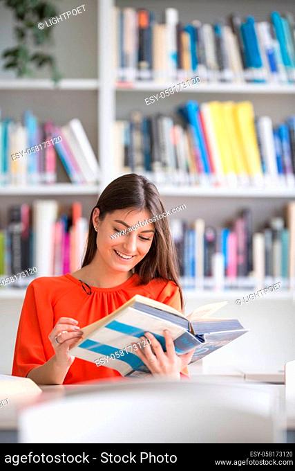 Pretty, young college student looking for a book in the library, studying for her exam