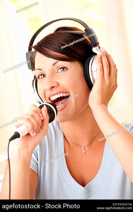 Closeup portrait of happy woman singing with microphone, holding on to headphones
