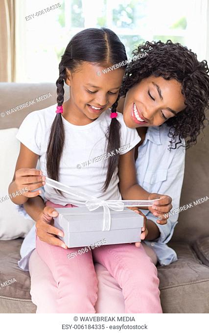 Pretty mother sitting on couch with daughter opening a gift