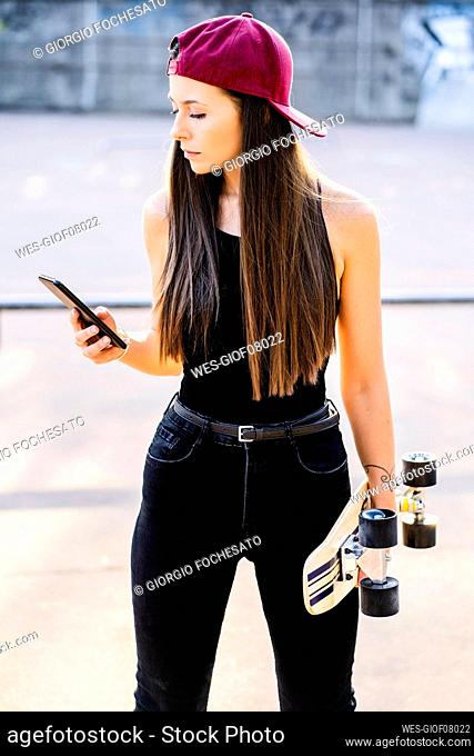 Young woman with smartphone and skateboard at skatepark