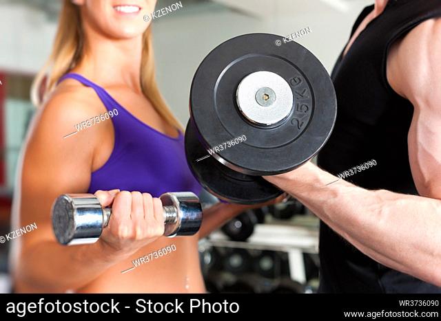 Young couple - man and woman - is exercising with barbell in gym to strengthen the muscles