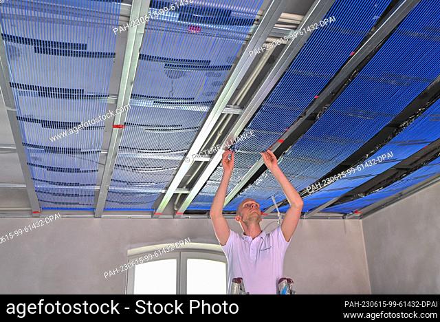 PRODUCTION - 14 June 2023, Brandenburg, Petersdorf: Emanuel Kaldun, employee of GeoClimaDesign AG, installs capillary tube mats on a ceiling that are used as...