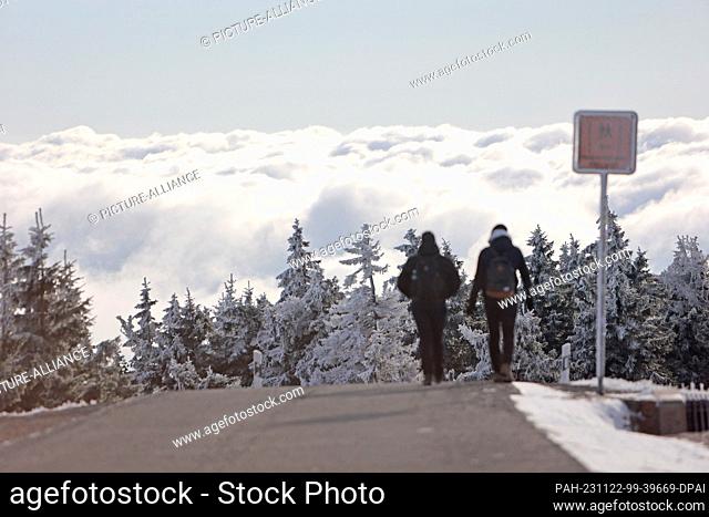 22 November 2023, Saxony-Anhalt, Schierke: Two hikers on the Brocken in front of a sea of clouds. The landscape in the Harz National Park on the Brocken is...