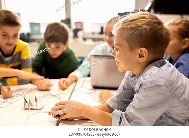 education, children, technology, science and people concept - group of happy kids with laptop computer playing and invention kit at robotics school lesson