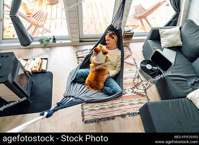 Woman with dog lying on hammock in living room at home