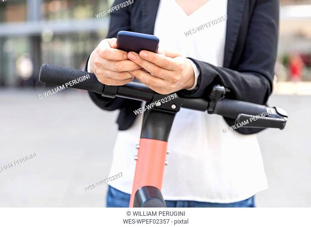Close-up of woman with e-scooter using smartphone in the city