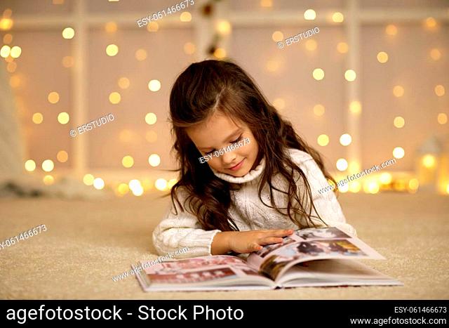 Happy curly little child girl is reading fairy tale book on the background with lights. Merry Christmas. space for text