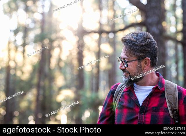 Man hiking and enjoying in a woods forest location. Side view of a man wearing a bag walking through a forest. Happy adult young caucasian male portrait...