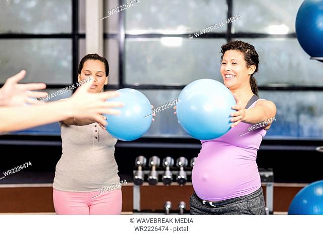 Pregnant women and trainer exercising with fitness ball