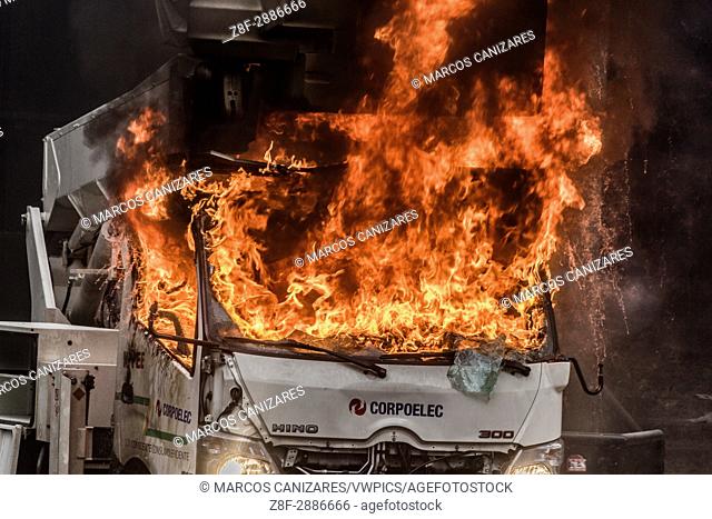 Protesters use ""Corpoelec"" car as a barricade at the entrance of the Supreme Court of Justice (TSJ) and burn it. An anti-government demonstrator is carried to...