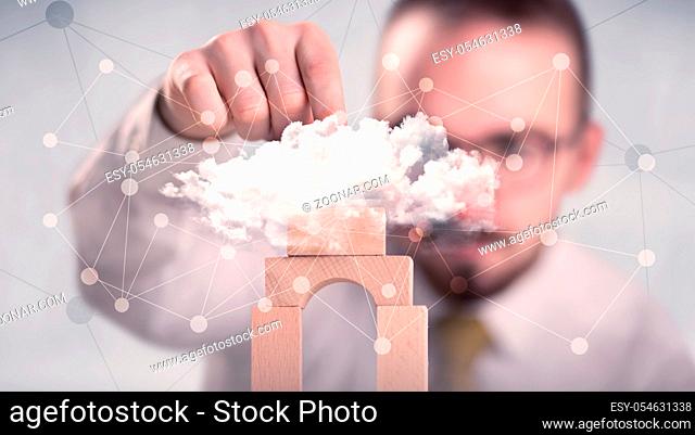 Young handsome businessman using wooden building blocks behind cloud concept