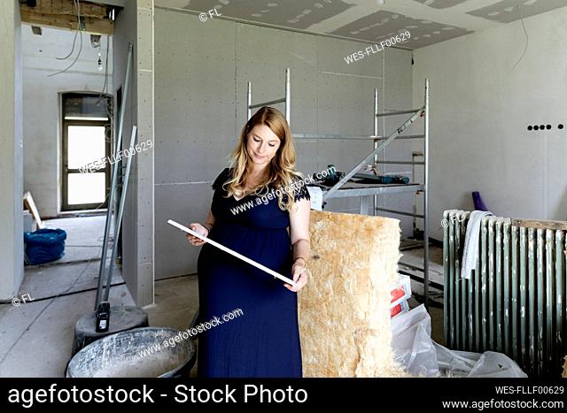 Pregnant woman holding wood plank at home under construction