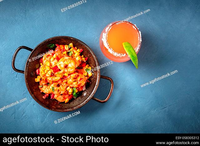 Spicy shrimps and a Paloma cocktail, shot from the top on a blue background with a place for text