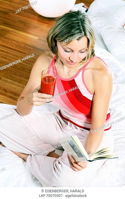 Young woman drinking fruit juice and reading a book