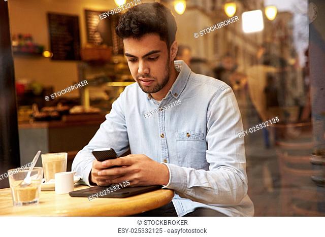 Man Viewed Through Window Of Café Using Mobile Phone