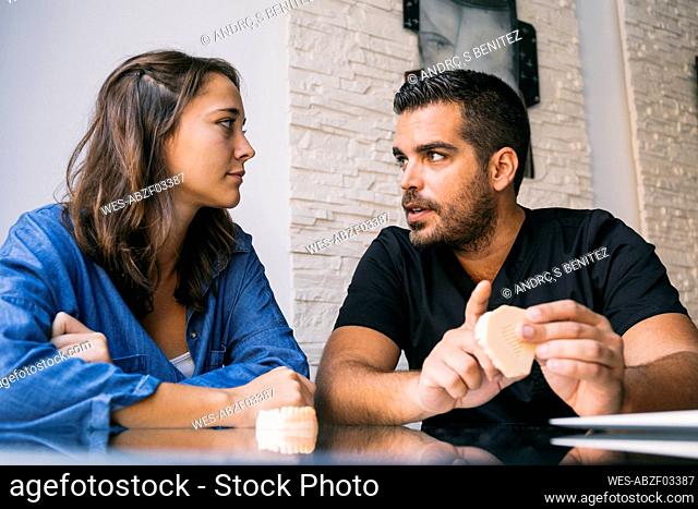 Handsome male dentist discussing with young female patient over gums model in office