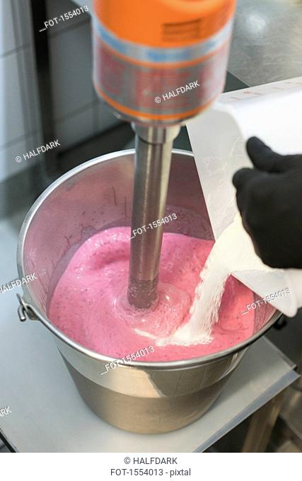 Detail of hand mixing ingredient into strawberry ice cream in machine