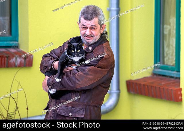 16 February 2021, Mecklenburg-Western Pomerania, Demmin: Torsten Lohr and the six-year-old tomcat Quarky in the courtyard of a residential building