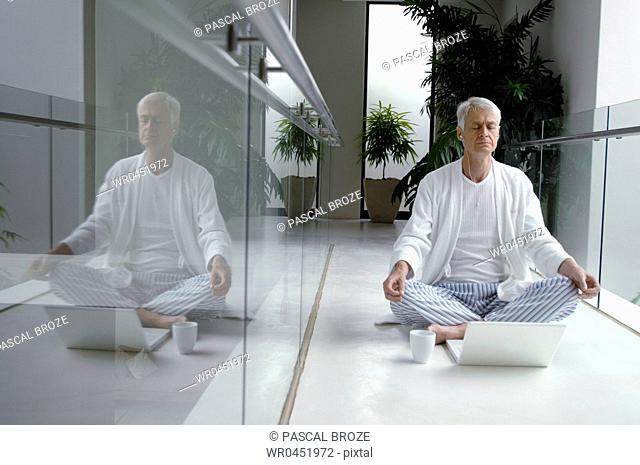Senior man doing yoga in front of a laptop