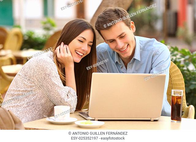 Happy couple watching social media in a laptop in a restaurant terrace