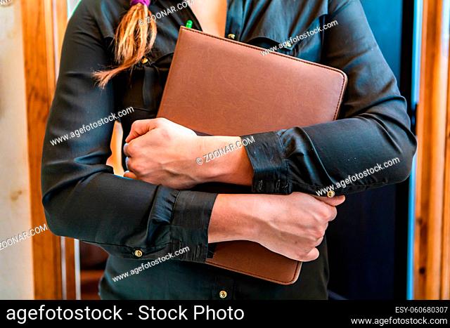 cropped close up view of unrecognizable young worker woman standing, hugging and holding her professional leather cover notebook with her arms