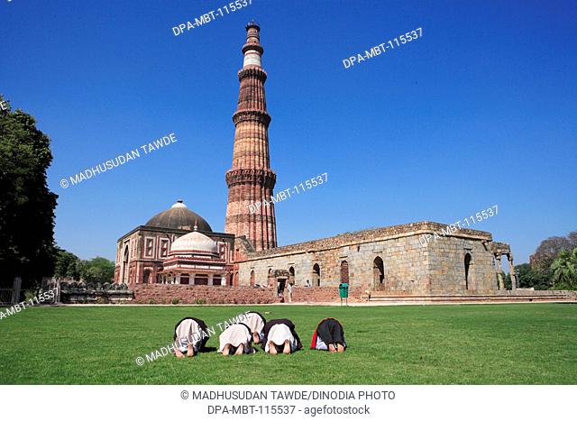 Children doing Namaz in front of Alai Darwaza , Imam Zamin's tomb and Qutab Minar built in 1311 red sandstone tower , Indo-Muslim art , Delhi sultanate , Delhi