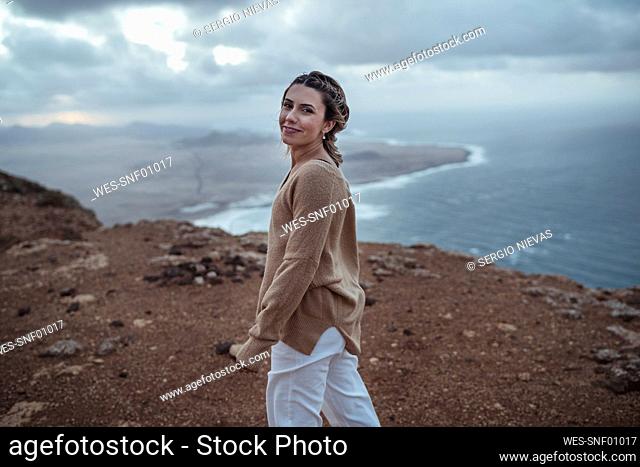 Young woman smiling while walking on mountain against Famara Beach, Lanzarote, Spain