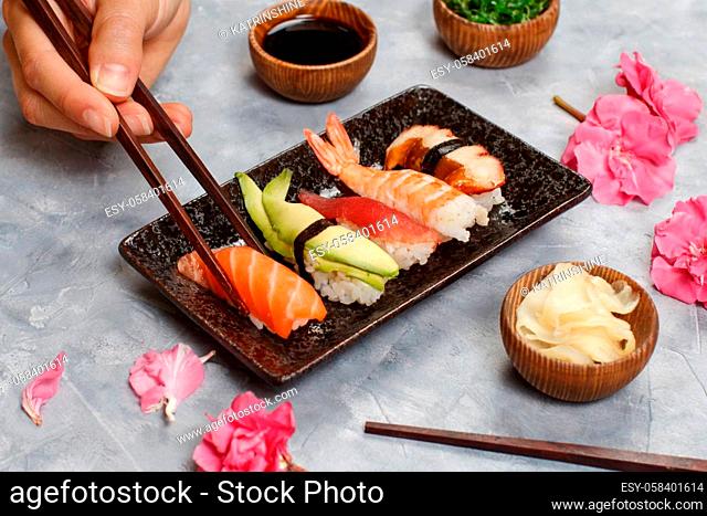 Close up of hand taking roll with chopsticks from a plate in sushi bar