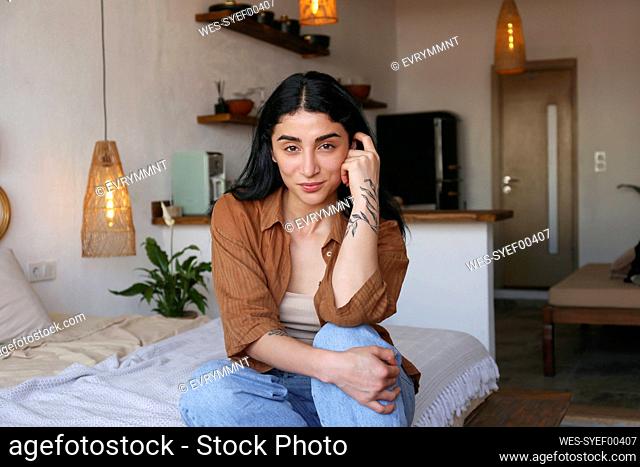 Smiling young woman sitting on bed at home