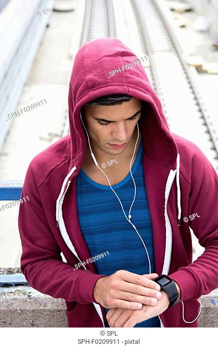 Young man wearing ear phones checking watch