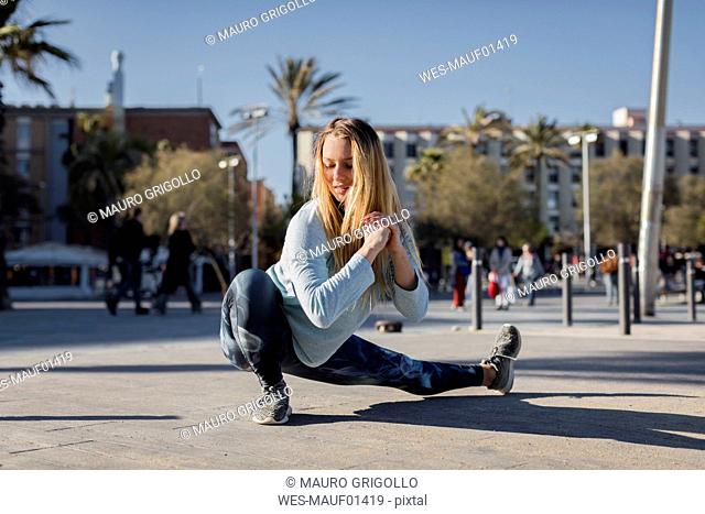 Spain, Barcelona, woman stretching leg on beach promenade