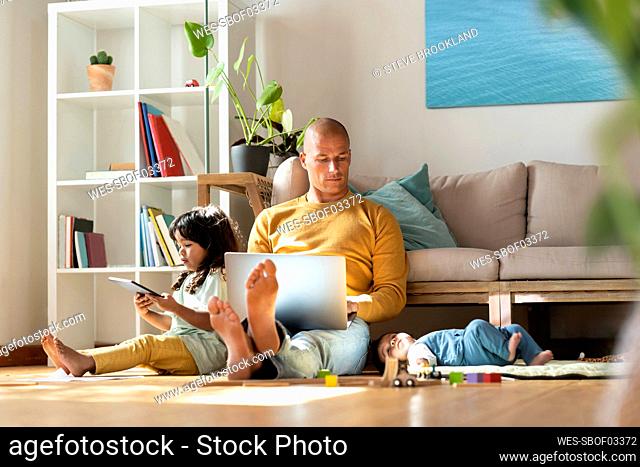 Father working on laptop while sitting by daughters at home