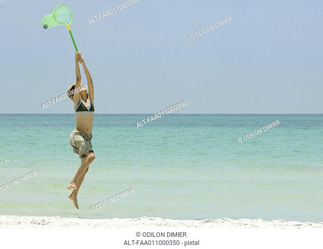 Girl jumping with fishing net on beach