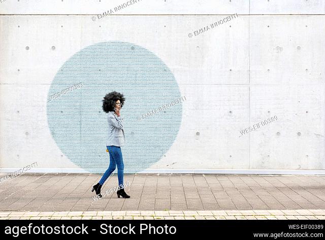 Visualization of data coming out of smart phone used by young woman walking along sidewalk
