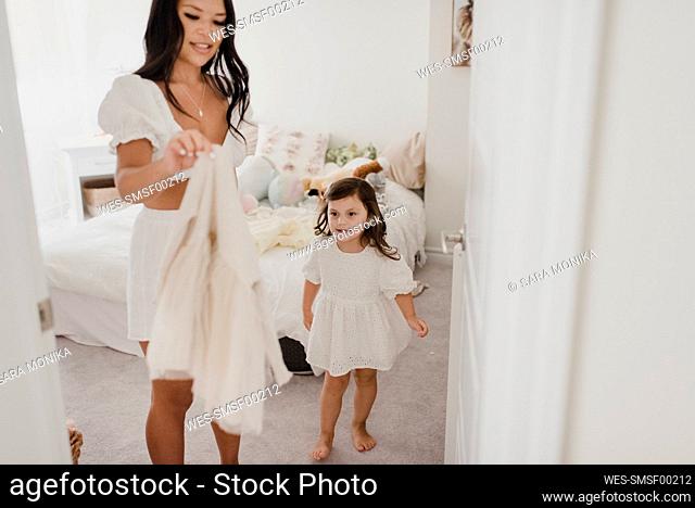 Smiling mother holding daughter's dress in bedroom