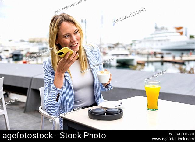 Businesswoman talking on speaker phone sitting at cafe