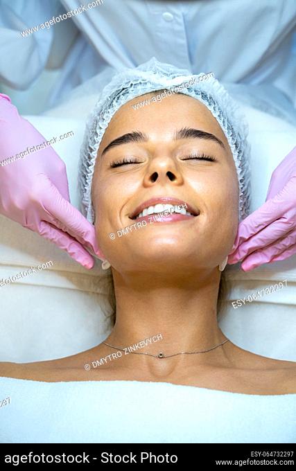 Unrecognizable female beautician doctor cleaning customer skin, make facial massage to woman patient