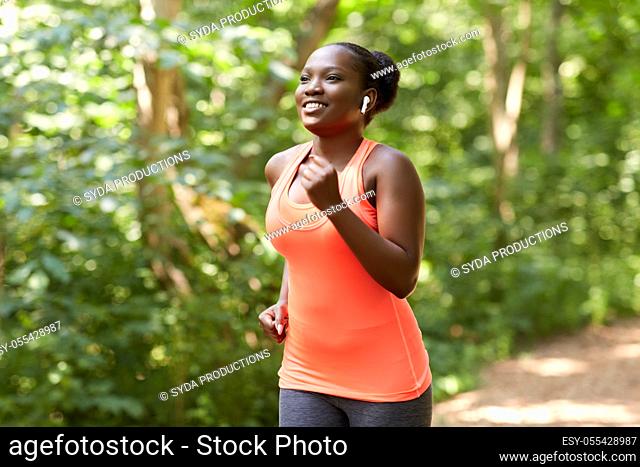 happy african woman in earphones running in park
