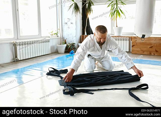 Mature aikido master folding kimono hakama after martial arts training class at gym of professional sport school
