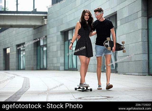 Young pair in love of stylish teenagers ride longboards tenderly hugging on in the industrial background