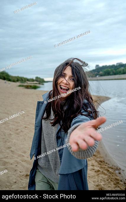 Happy woman wearing blue raincoat gesturing at shore