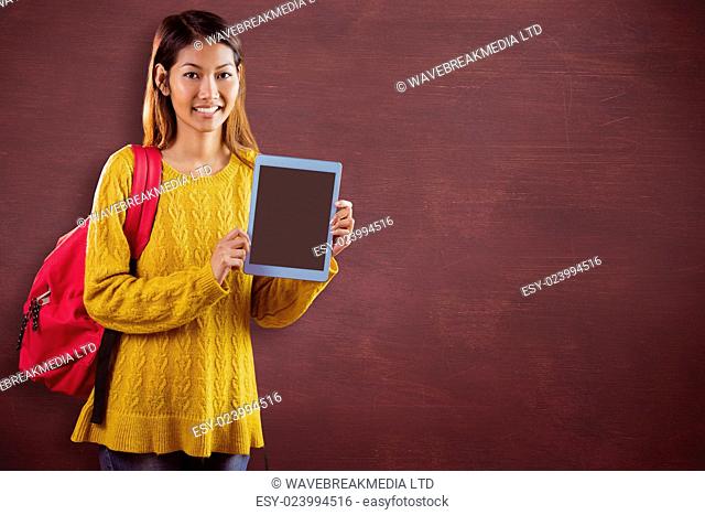 Smiling asian female student showing tablet against desk